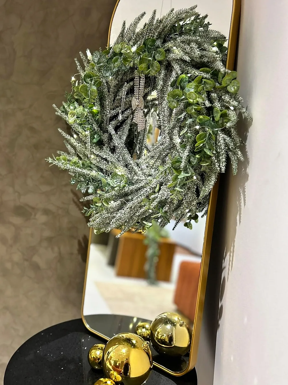 Frosted wreath on an arched gold mirror above mirror-gold baubles