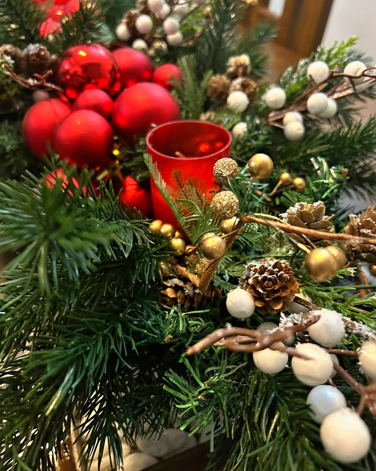 Table centrepiece of red baubles, a red candle, berries and pine cones